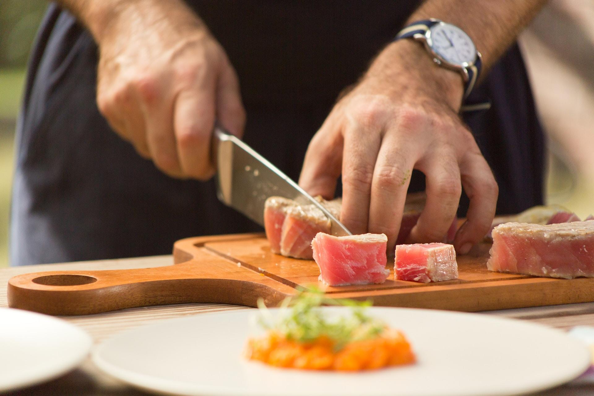 homme découpant une viande sur une planche