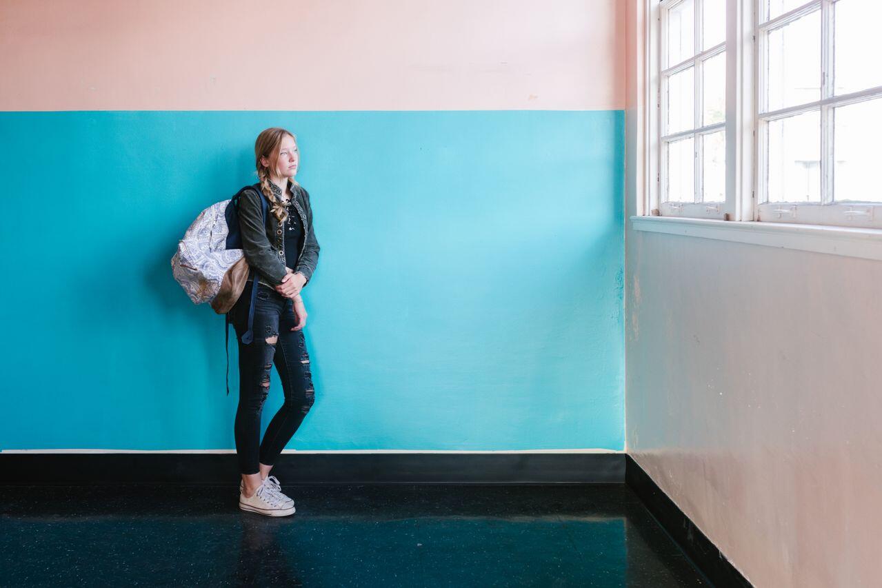 ado avc son sac contre un mur bleu regardant la fenetre