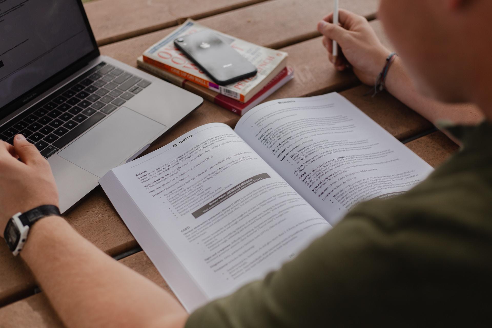 jeune homme révisant avec un livre devant son ordinateur