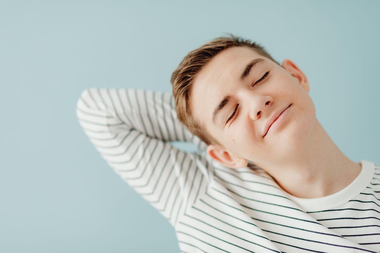 jeune adolescent s etirant devant un mur bleu ciel les yeux fermes et le sourire apaise