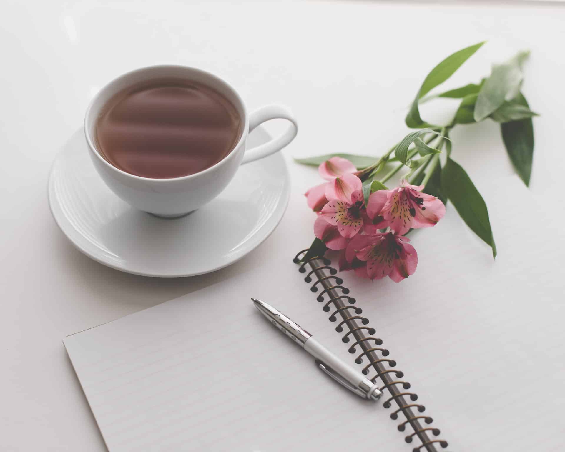 tasse de thé et fleurs poses sur une table pour accompagner carnet et stylo