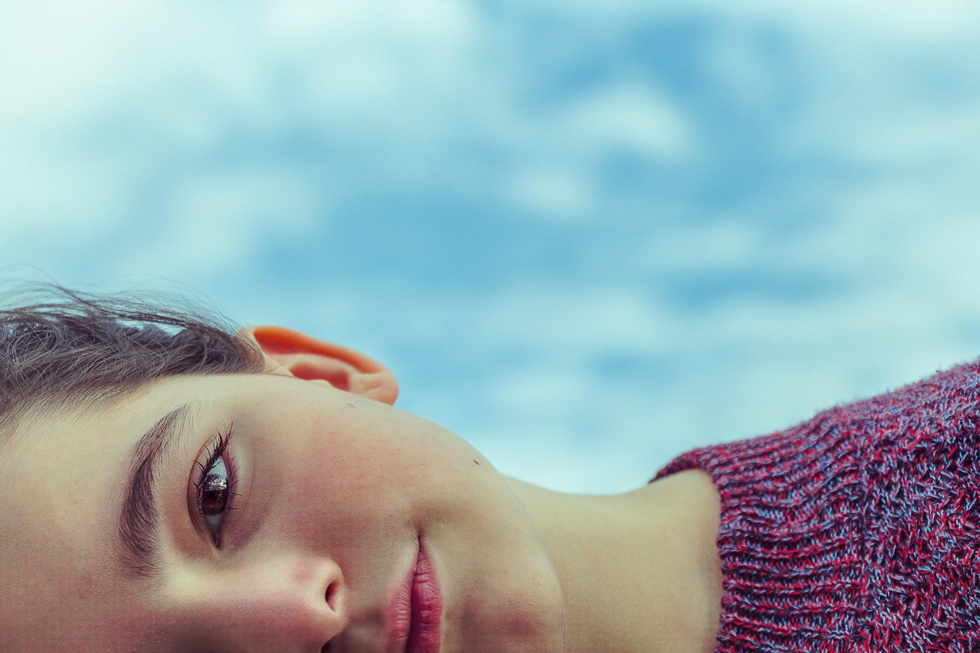 jeune fille allongée sous un ciel bleu rempli de nuages blancs