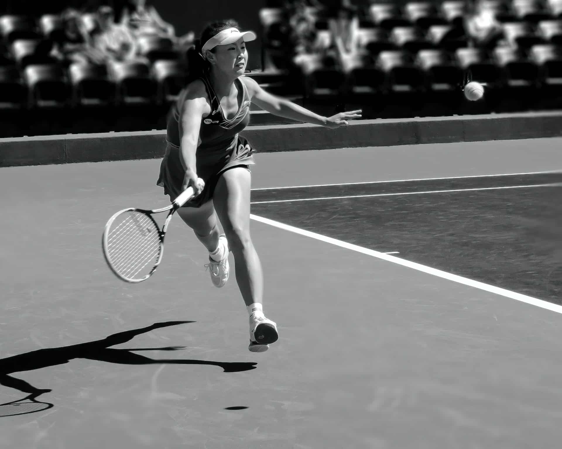 photo en noir et blanc d une joueuse de tennis courant pour rattraper la balle durant un match