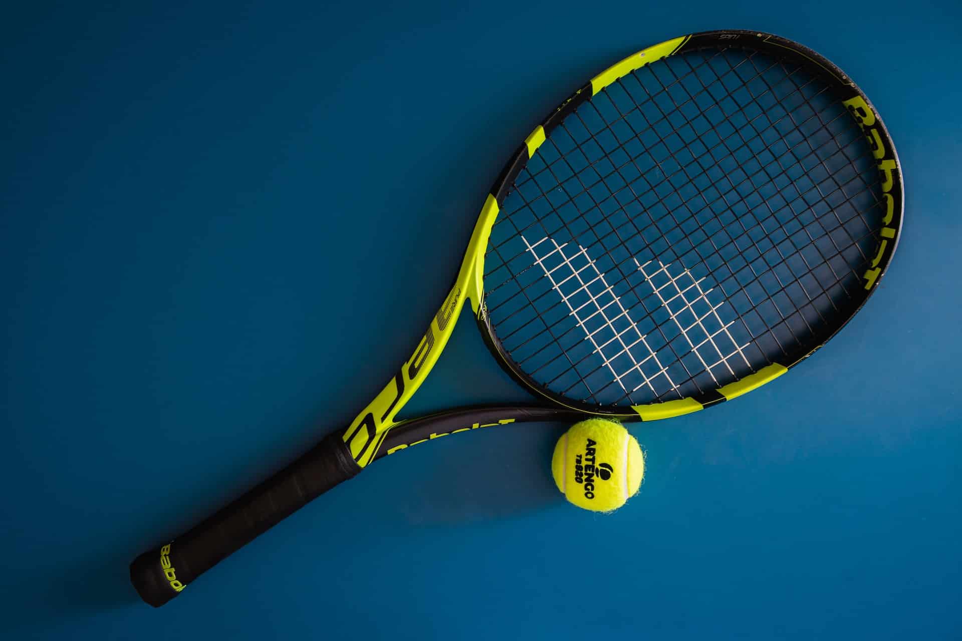 raquette de tennis et sa balle disposées sur un terrain bleu