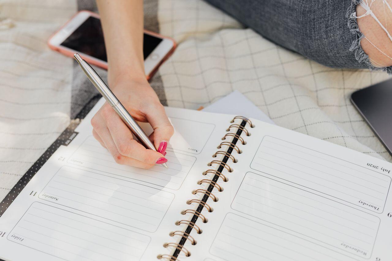 jeune femme avec vernis a ongle rose ecrivant dans son agenda