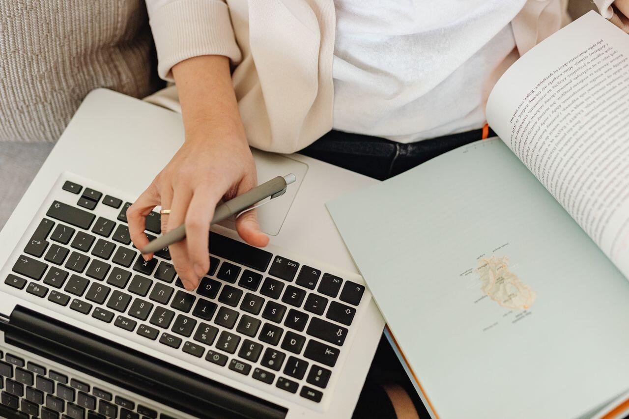 personne en blazer avec un livre, un stylo et un clavier