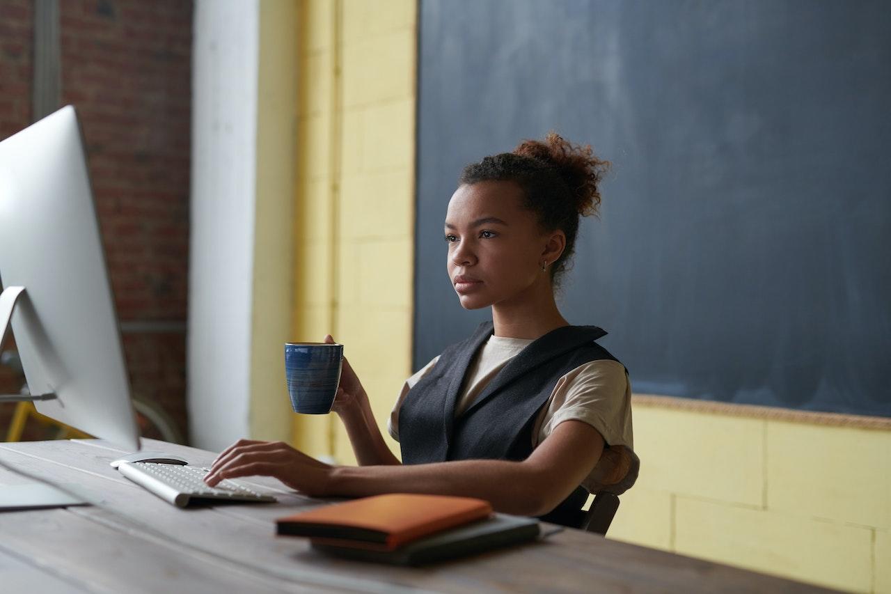 jeune prof assise derriere un tableau noir avec une tasse de the