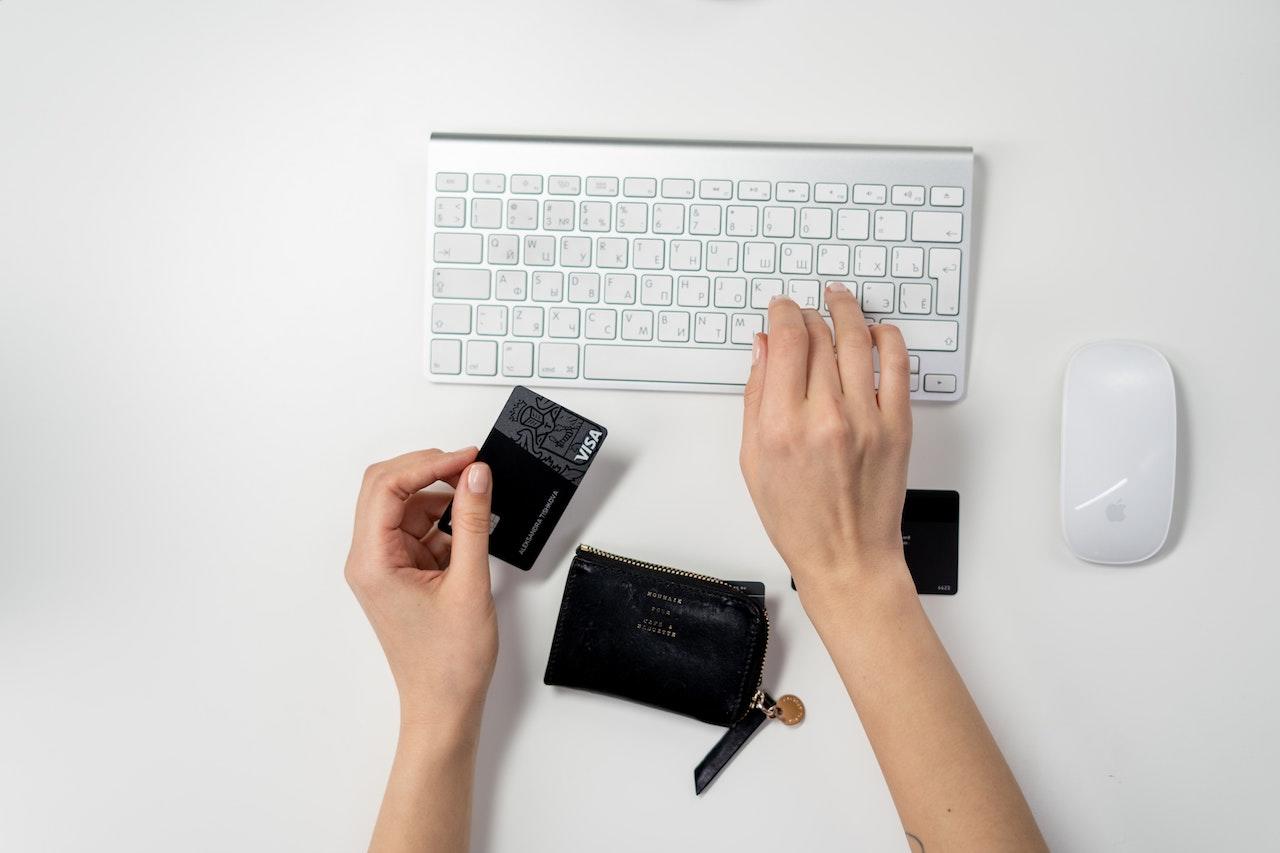 mains tapant sur un clavier tout en tenant une carte de credit