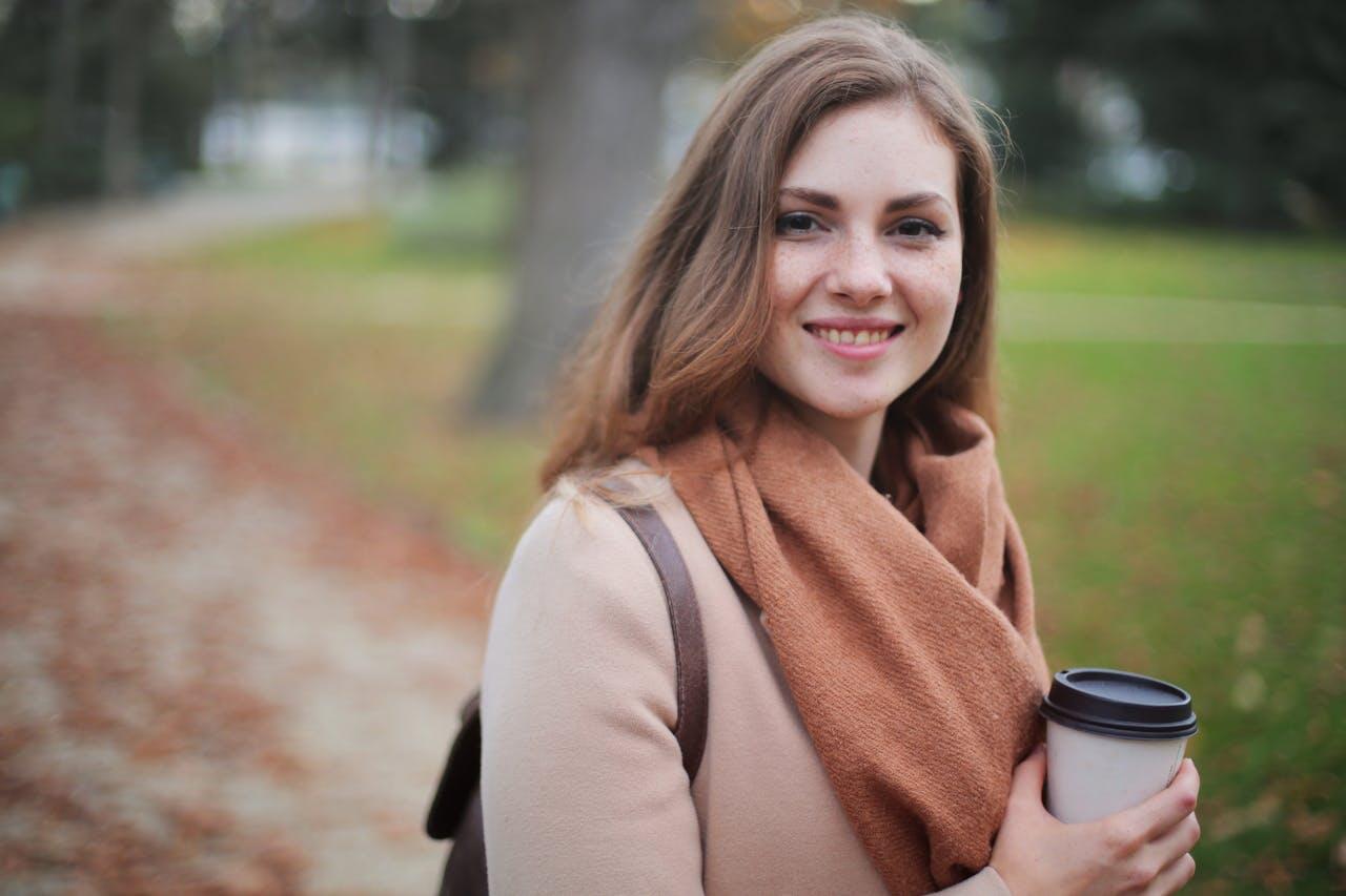 jeune femme souriant dehors avec son cafe