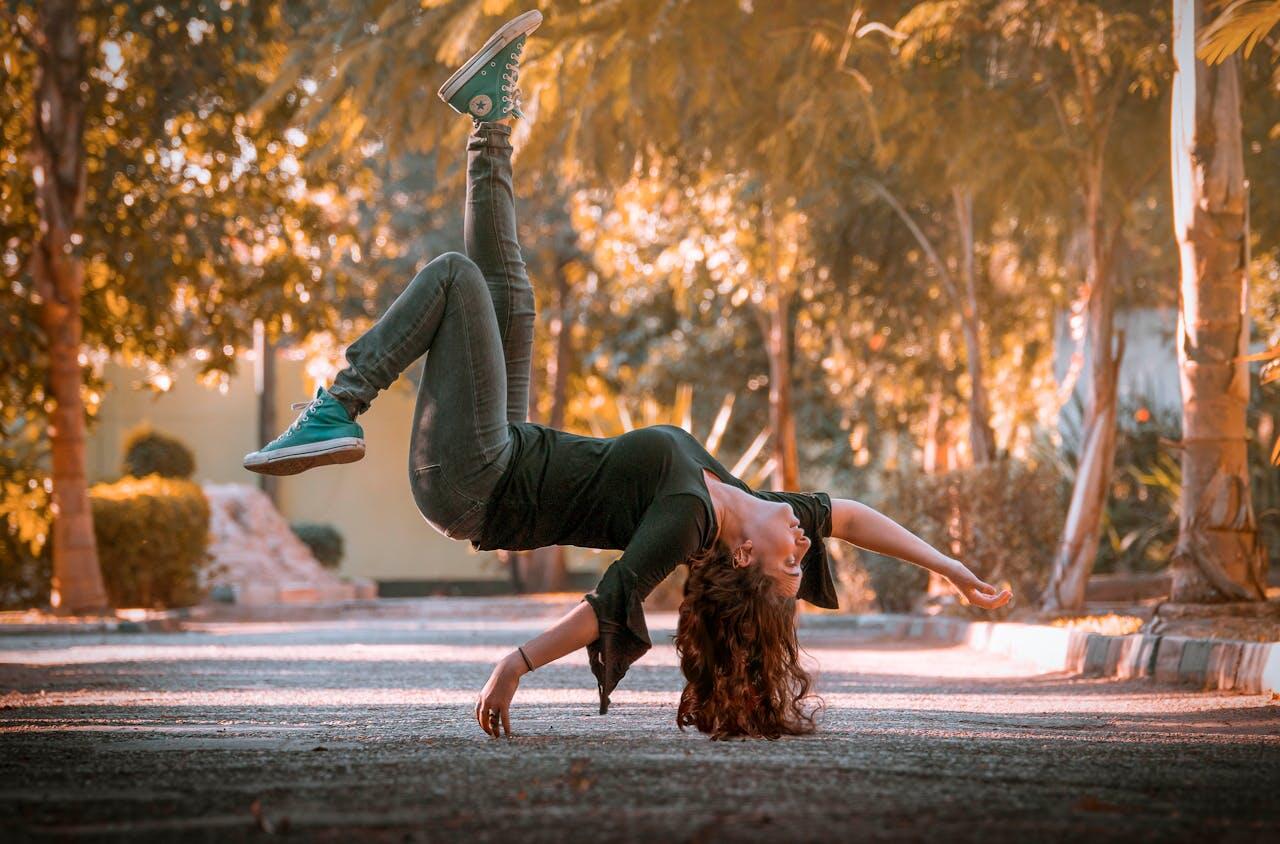 jeune femme sur la route au milieu des arbres effectuant un mouvement de danse au sol