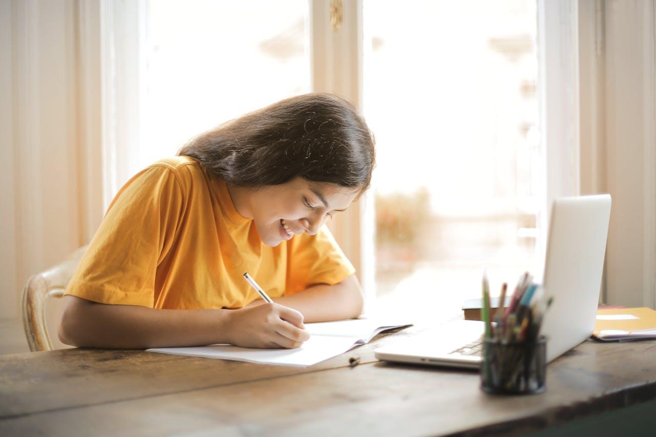 jeune fille a la maison en tte shirt jaune orange etudiant avec un carnet et un ordi sur une table