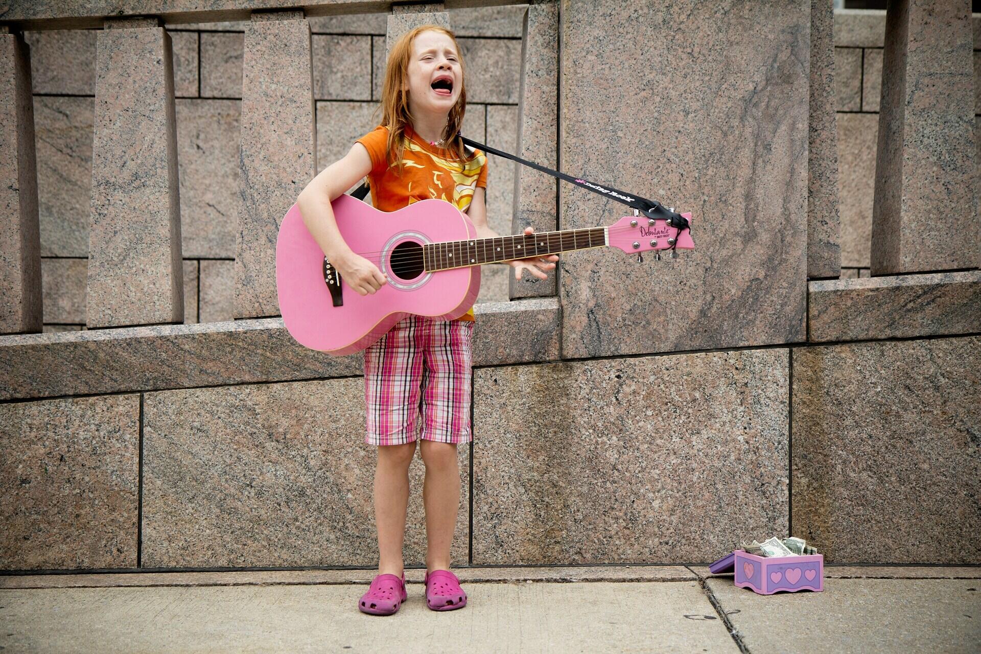 Criança tocando com uma guitarra rosa.