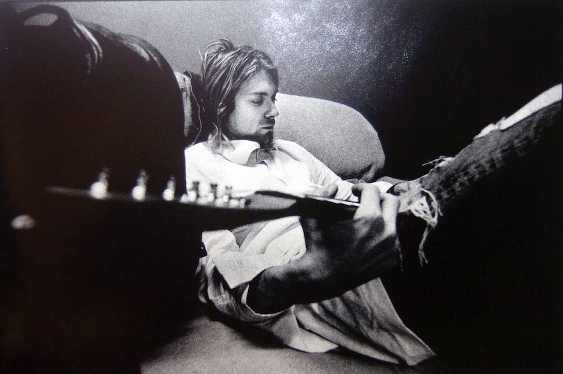 Kurt Cobain sentado, tocando guitarra.