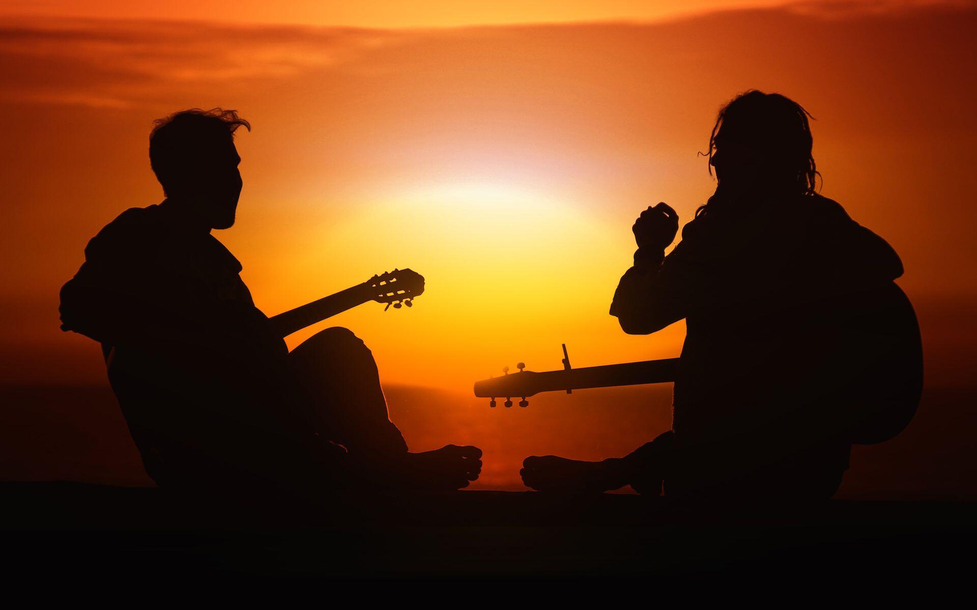 Duas pessoas tocando guitarra no pôr do sol