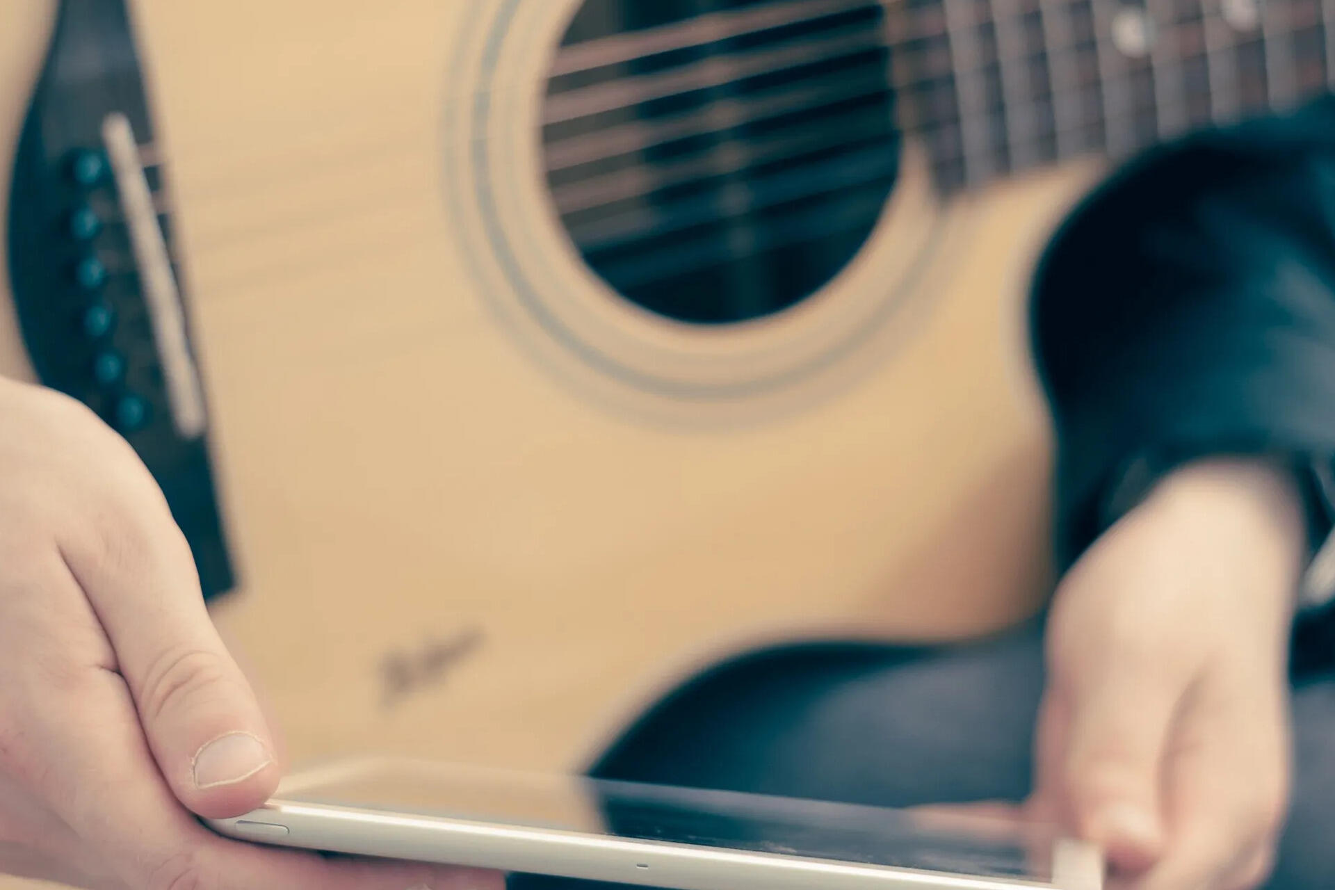 Pessoa segurando um celular e uma guitarra.