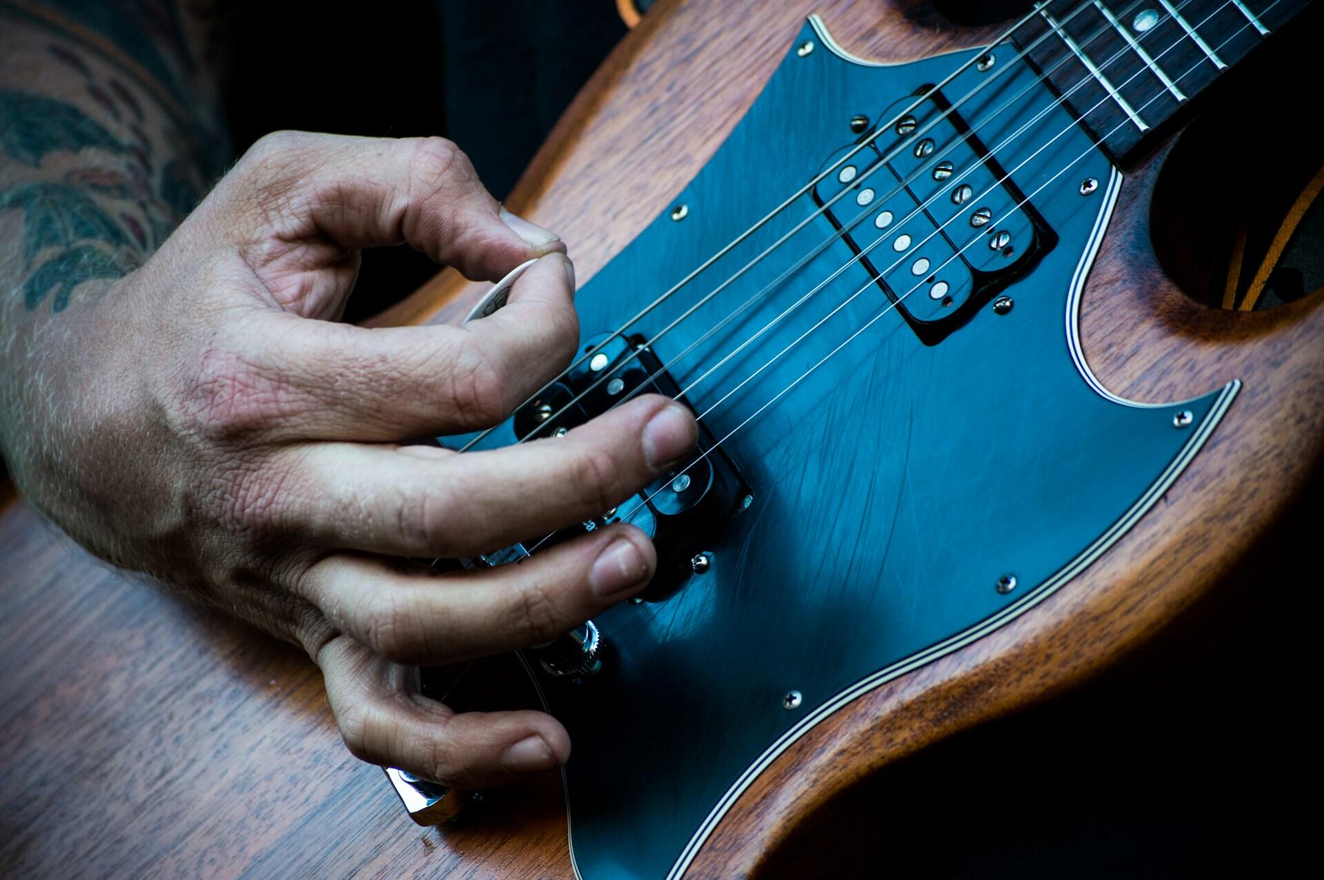 Homem tocando guitarra com uma palheta.