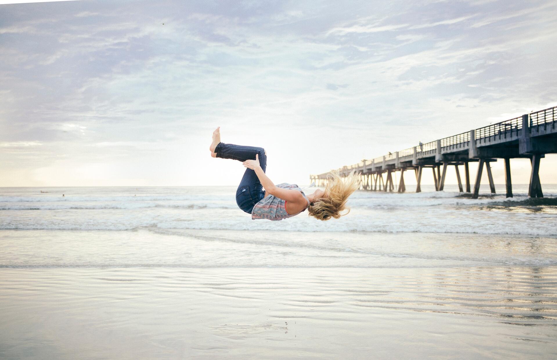 Mulher fazendo uma acrobacia numa praia.