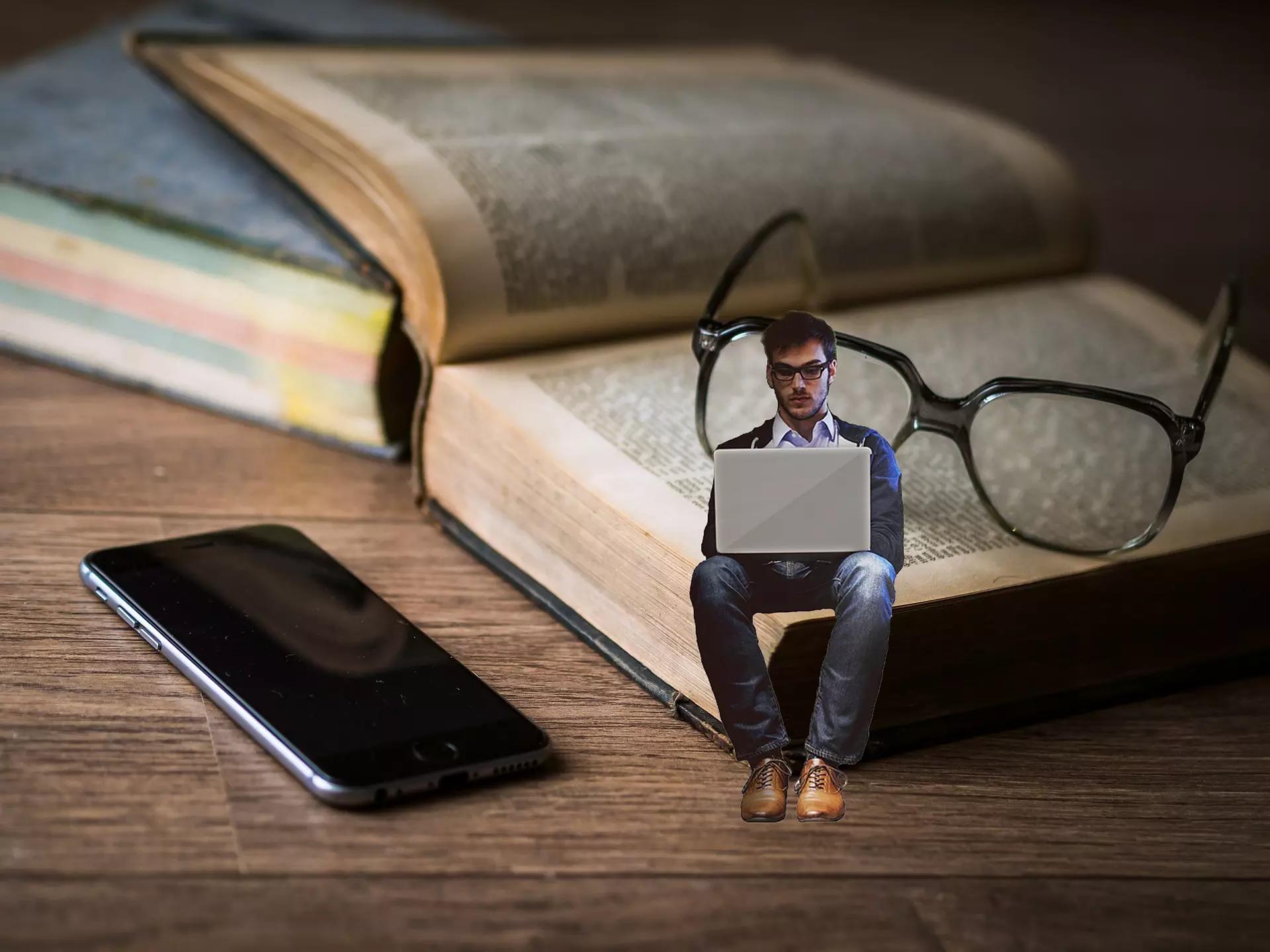 Homem em miniatura sentado sobre um livro aberto.