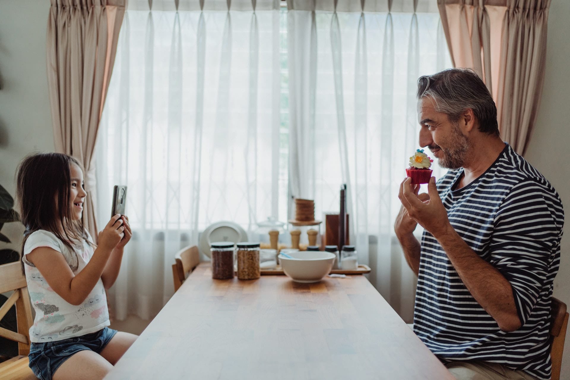 Menina fotografando o pai à mesa
