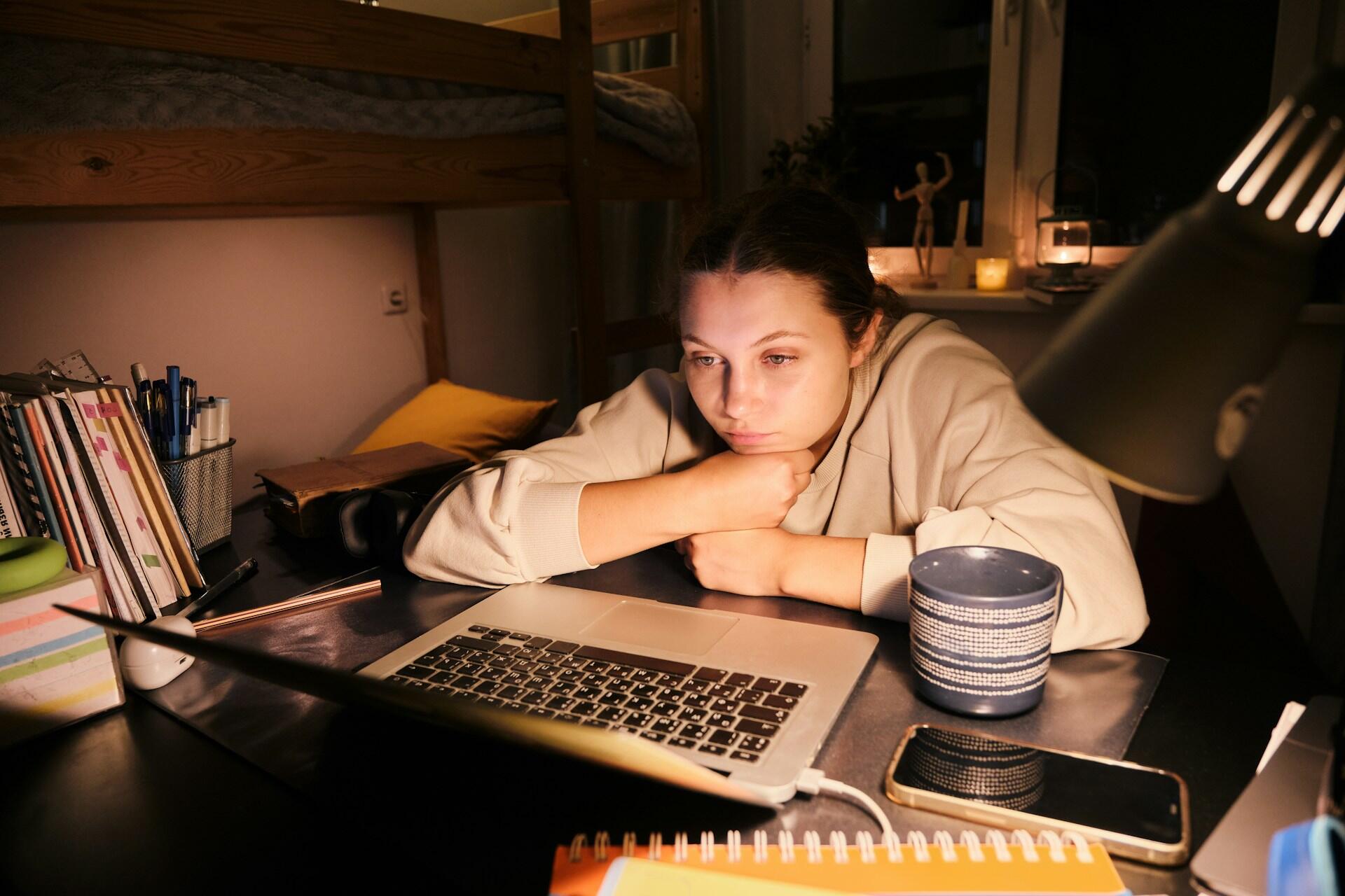 Menina na frente de um computador a noite, com aparência de preocupada e concentrada