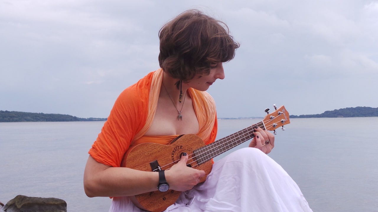 Uma mulher tocando ukulele com o mar no fundo