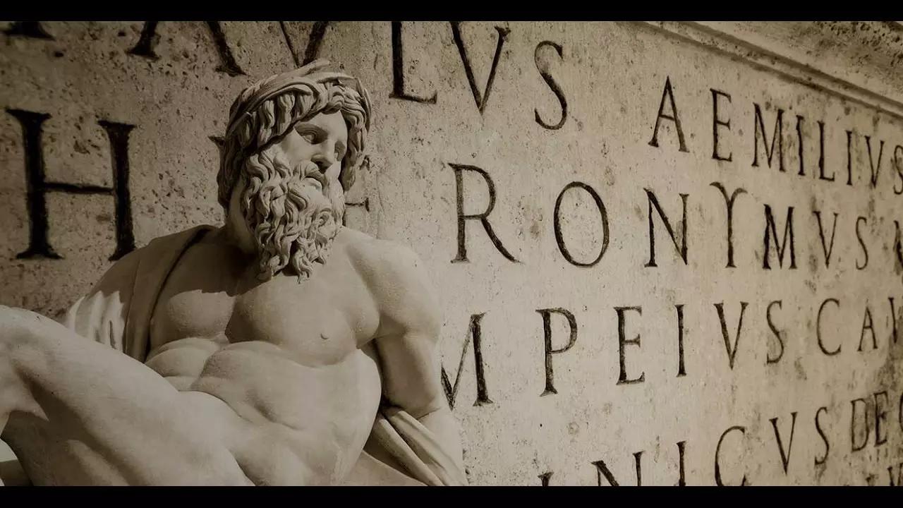Imagem de uma estátua em frente a um painel escrito em latim.