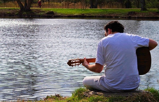 Homem toca violão na beira do lago.