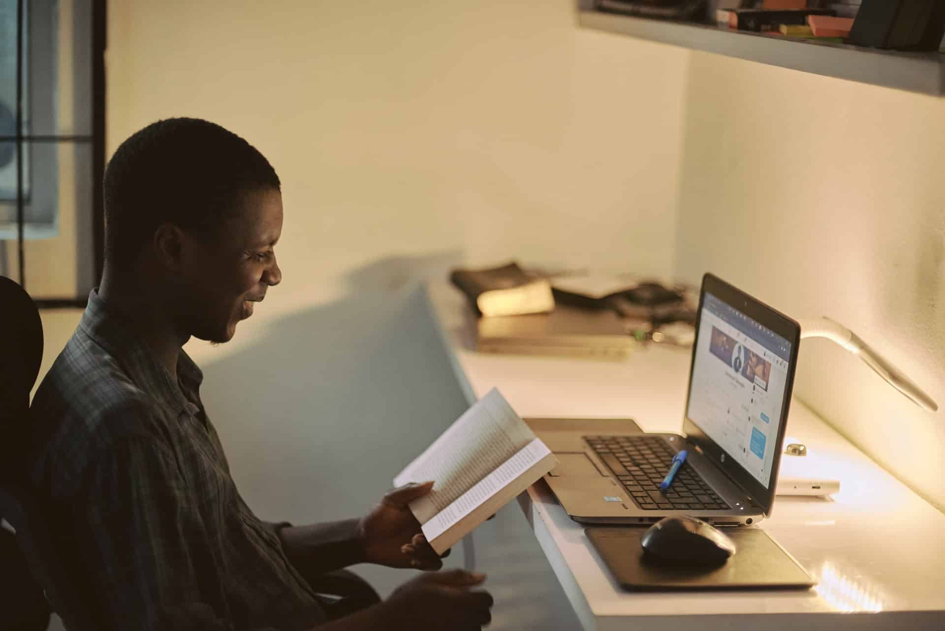 Homem negro lendo livro e vendo página internet