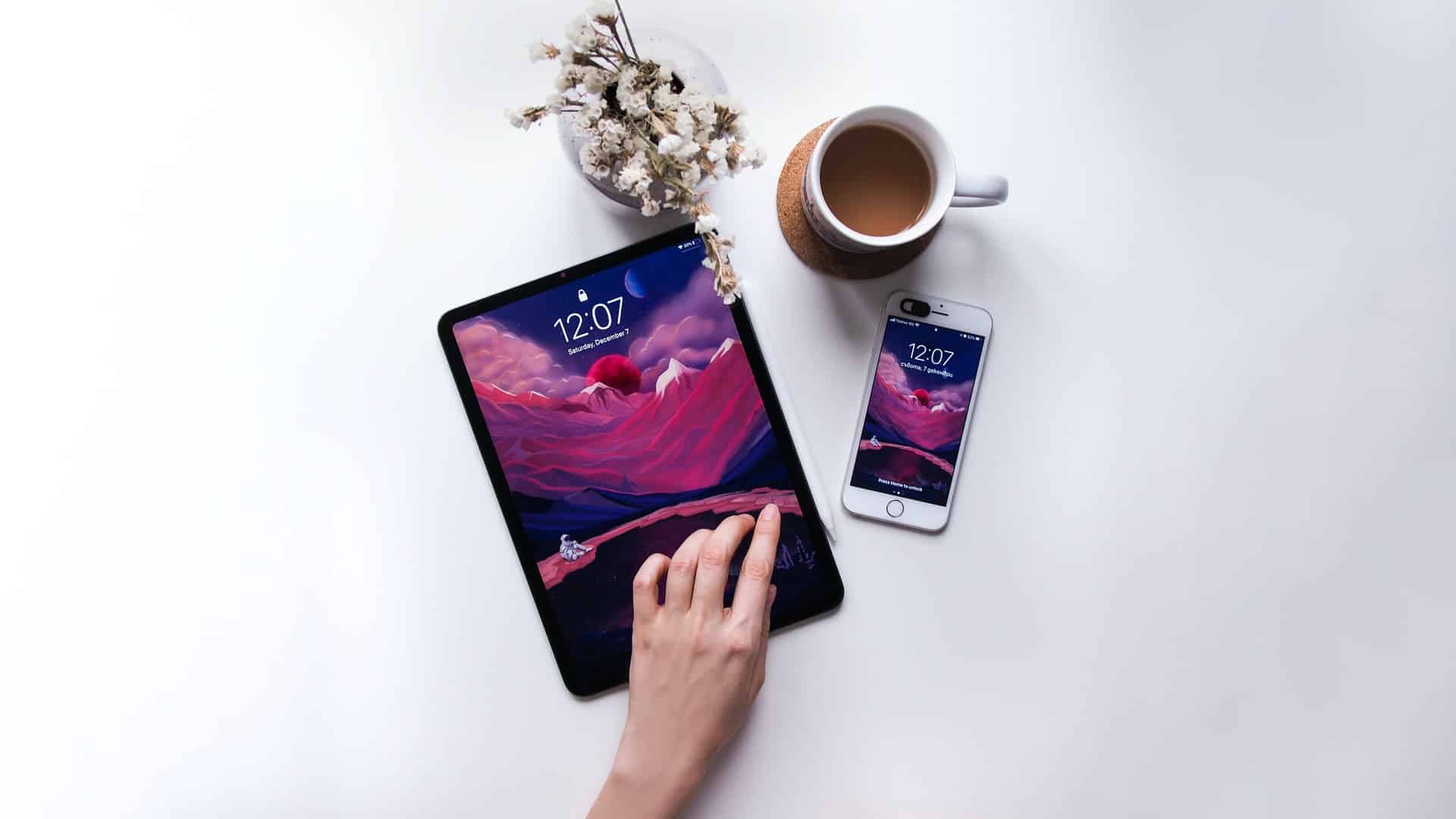 tablete e telefone expostos em mesa branca com uma taça de café