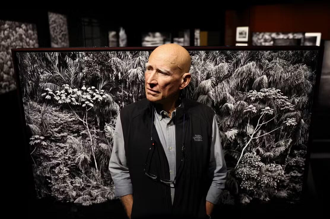 Foto do Sebastião Salgado em exposição com uma de suas obras