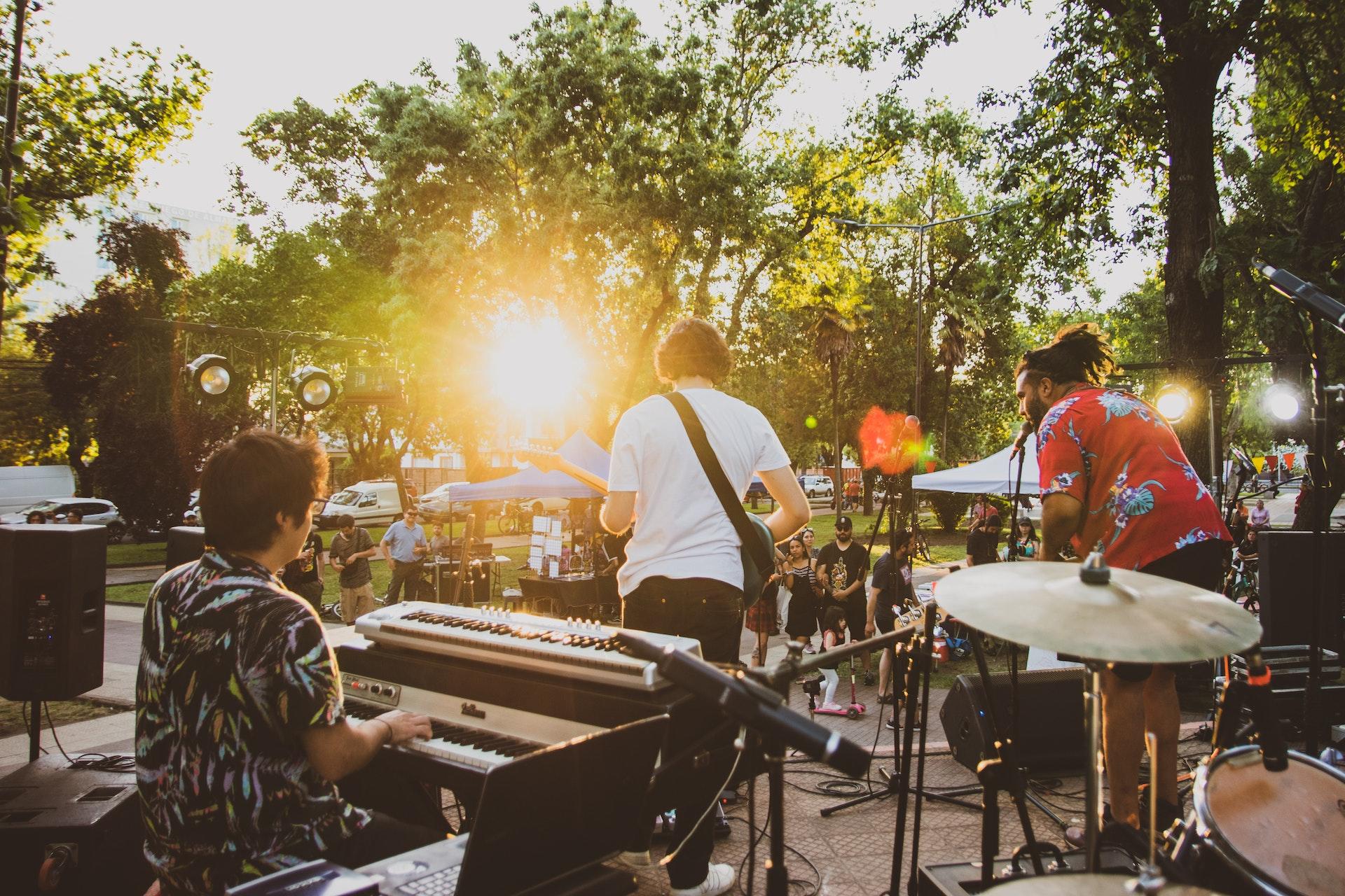 Banda em um palco diurno à luz do sol. No destaque, aparece um pianista. 
