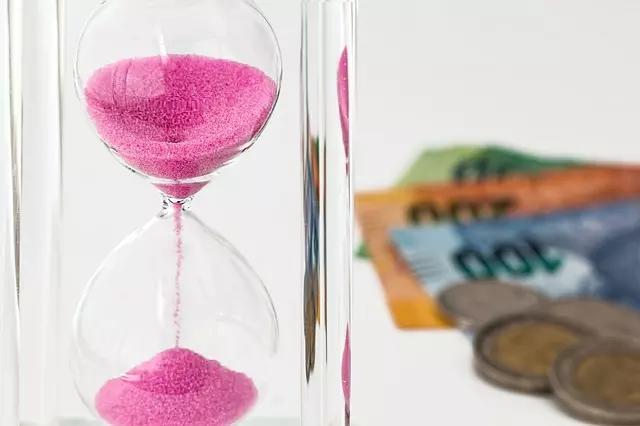 Uma ampulheta calcula o tempo com notas e moedas ao fundo.