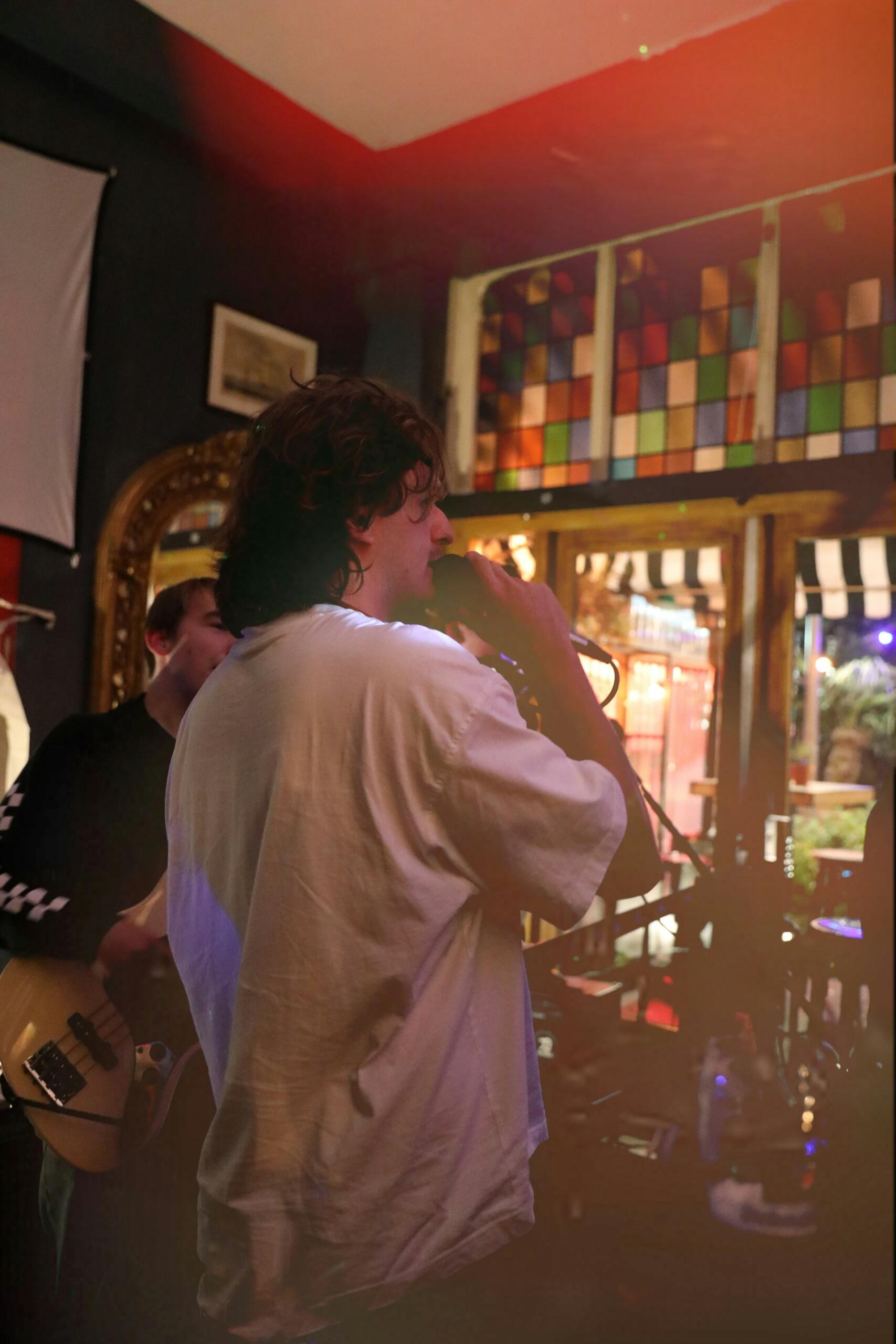 Homem cantando em um karaoke de bar, de costas pra imagem