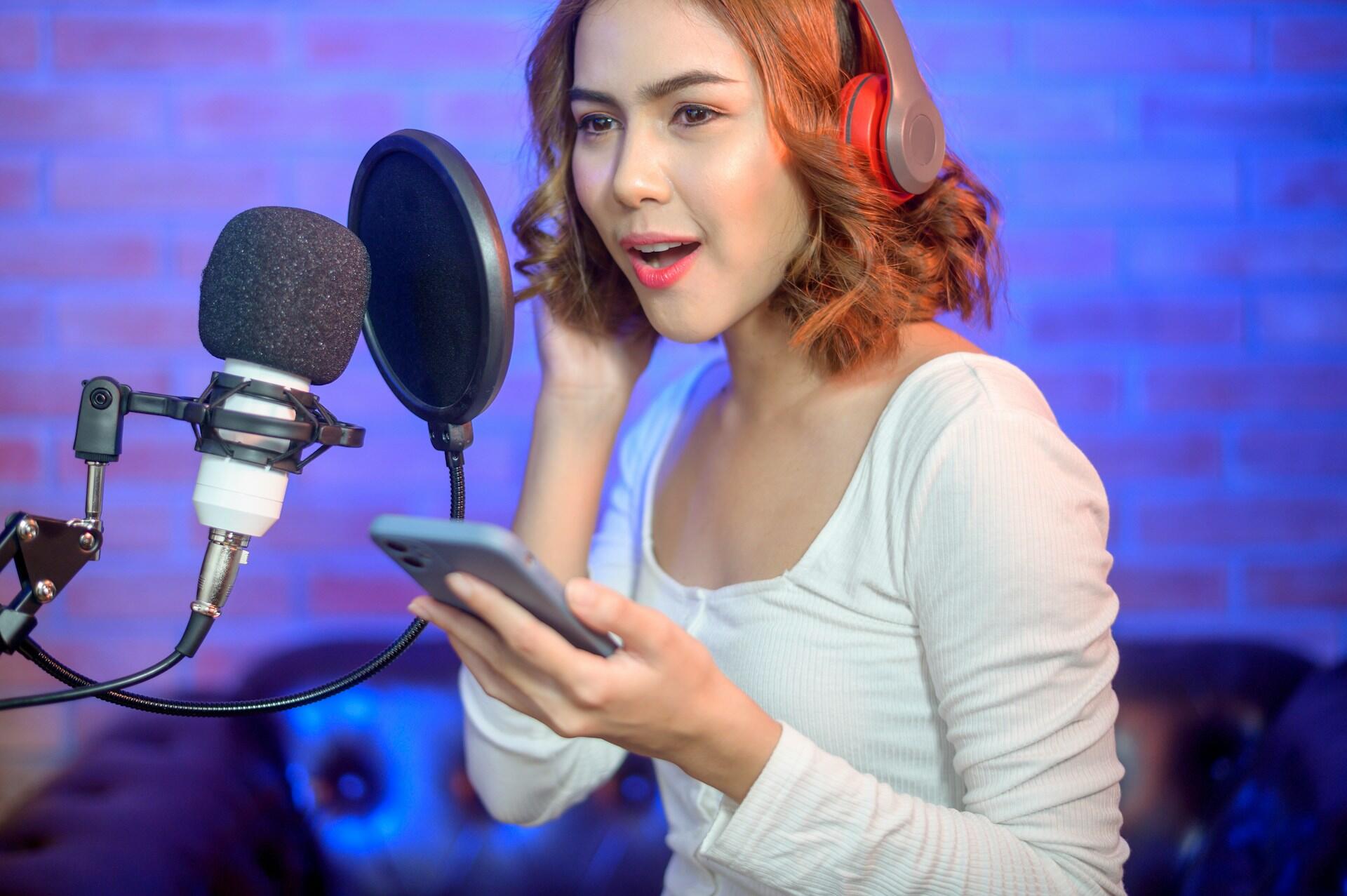 Moça ruiva gravando em um studio com microfone e celular