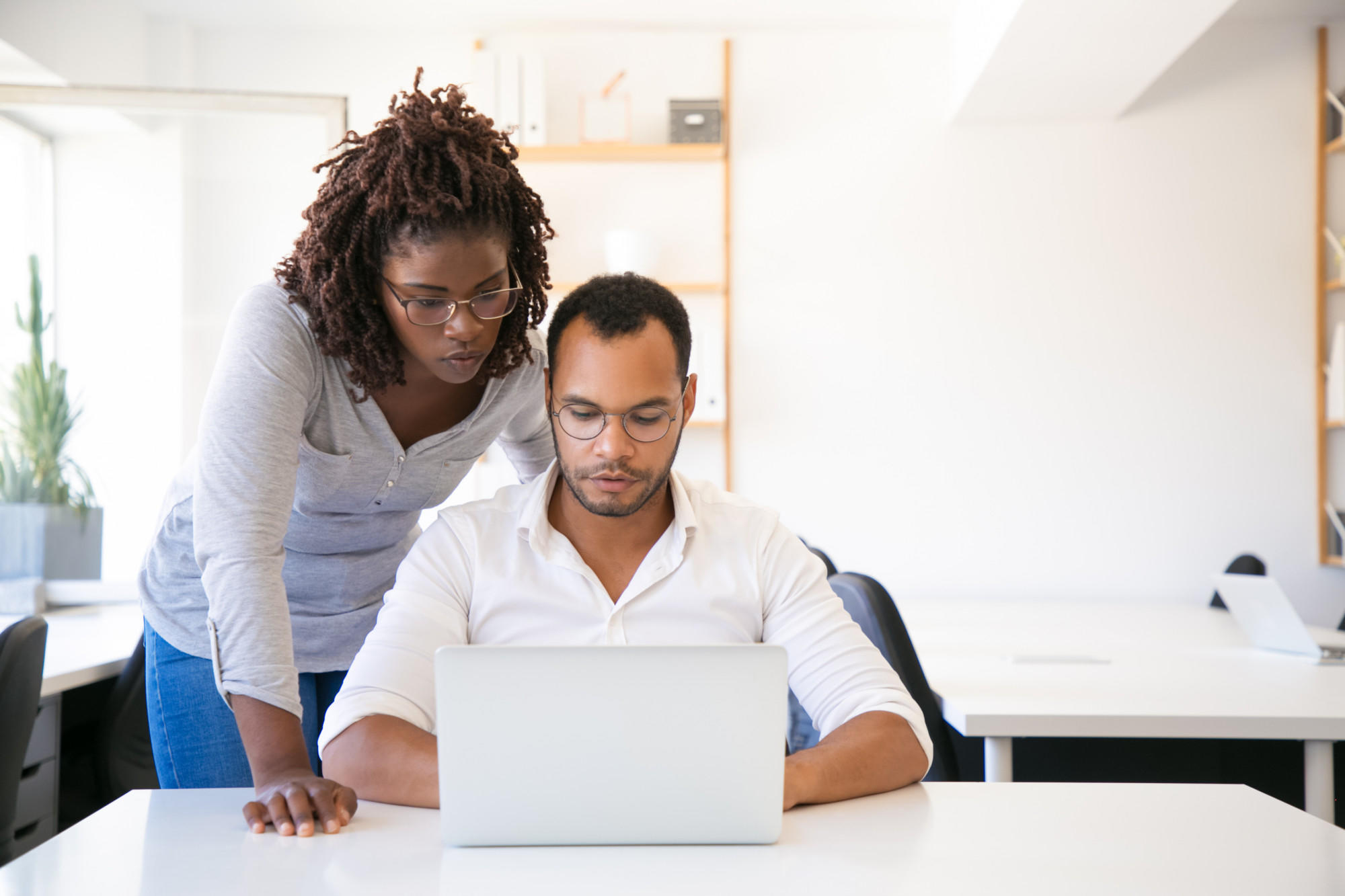 homem sentando em uma mesa olhando para um computador com uma mulher em pé orientando ao lado