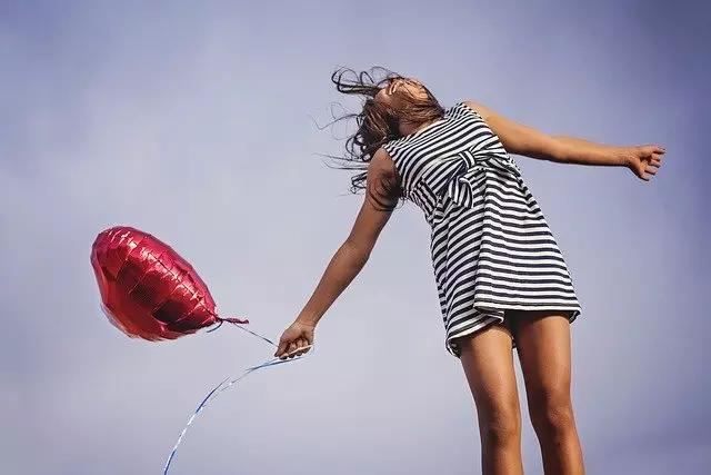 Mulher feliz segurando um balão vermelho em formato de coração.