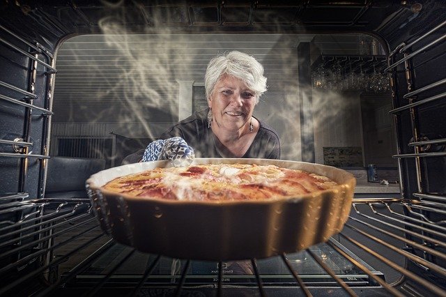 Senhora tira torta quente do forno.