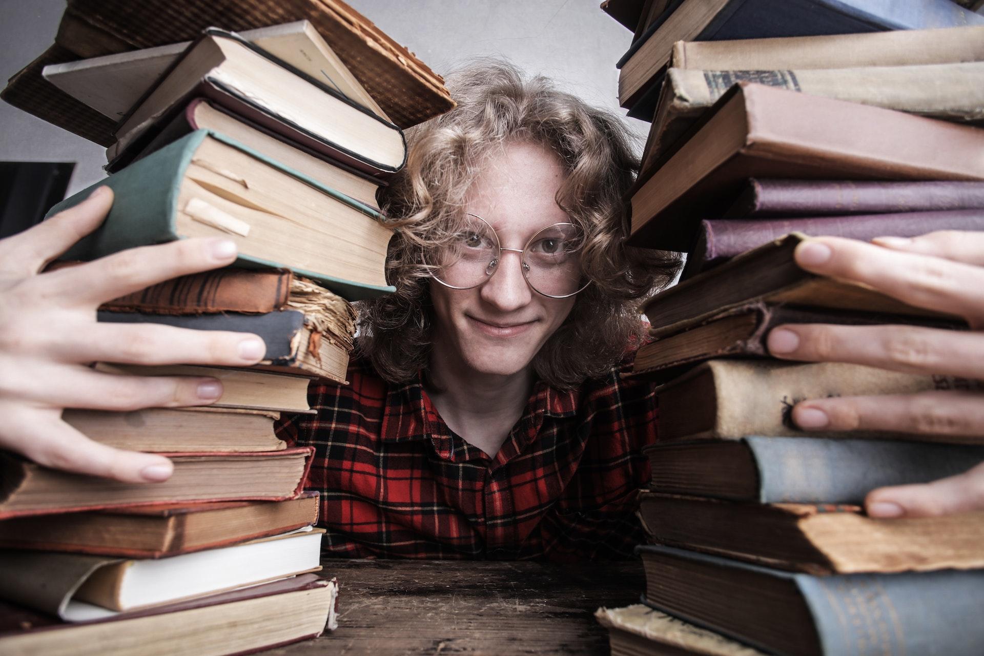 Jovem abraça duas pilhas de livros antigos.