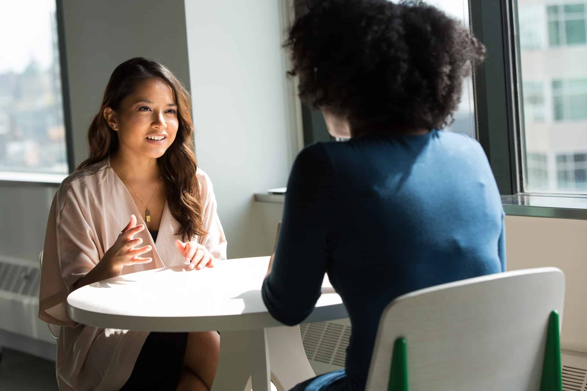 mulheres conversando de frente uma para a outra em uma mesa