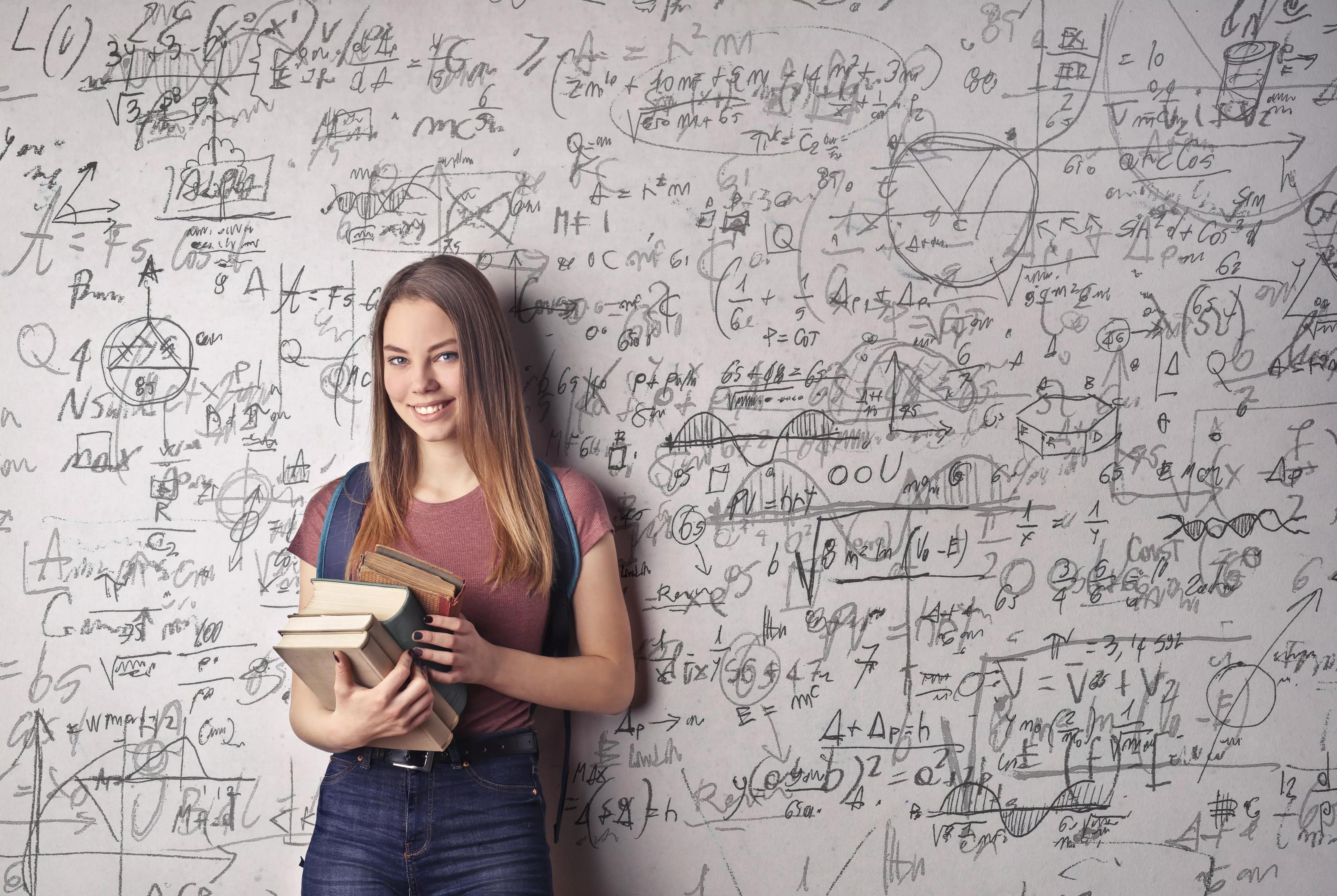 Uma menina encostada em uma parede cheia de inscrições matemáticas