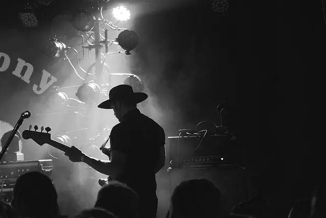 Homem tocando baixo em palco iluminado.