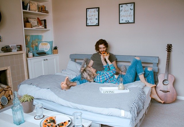 Casal come pizza e toca violão na cama