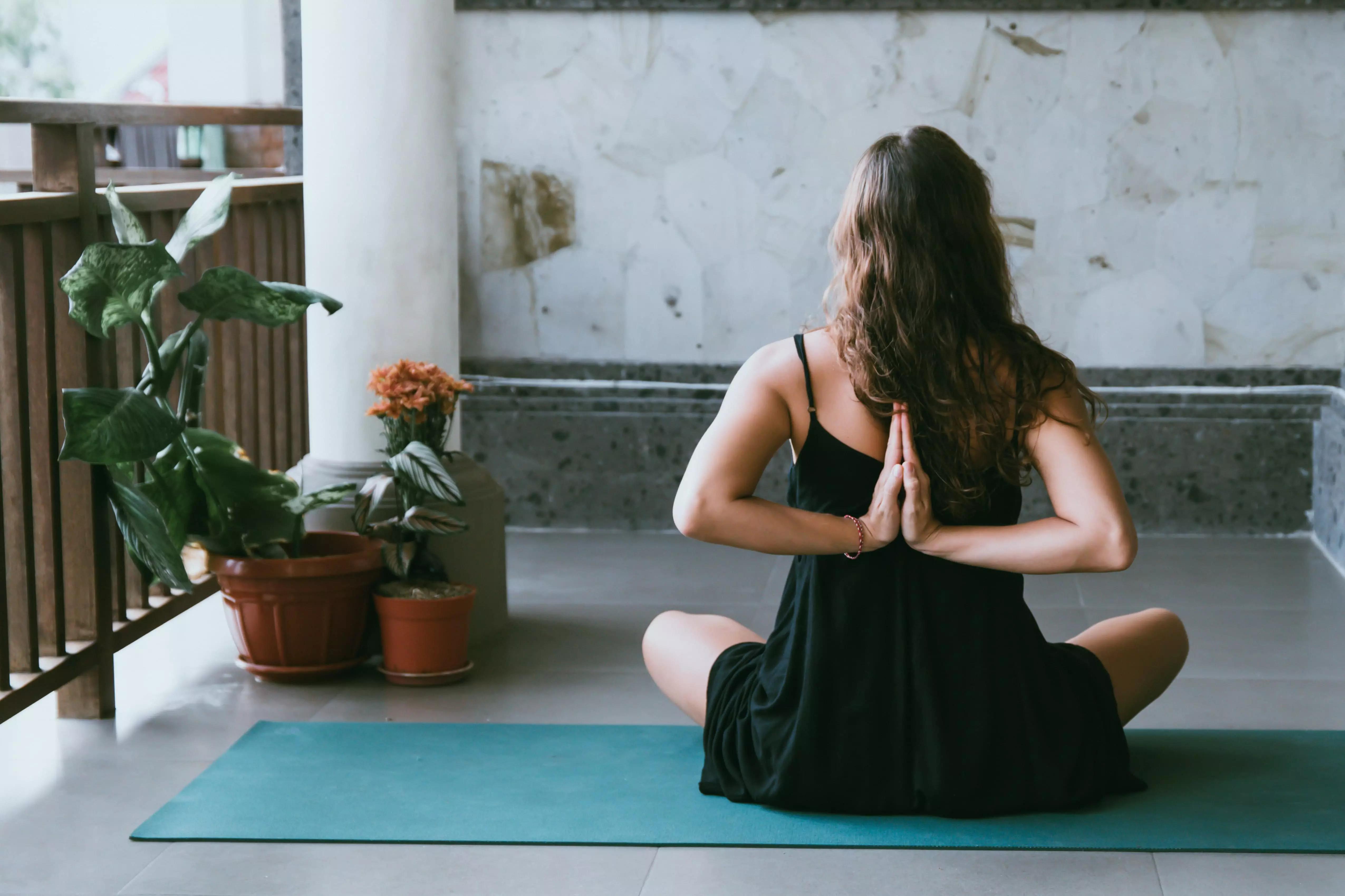 Uma mulher praticando yoga e fazendo um ássana num quintal.