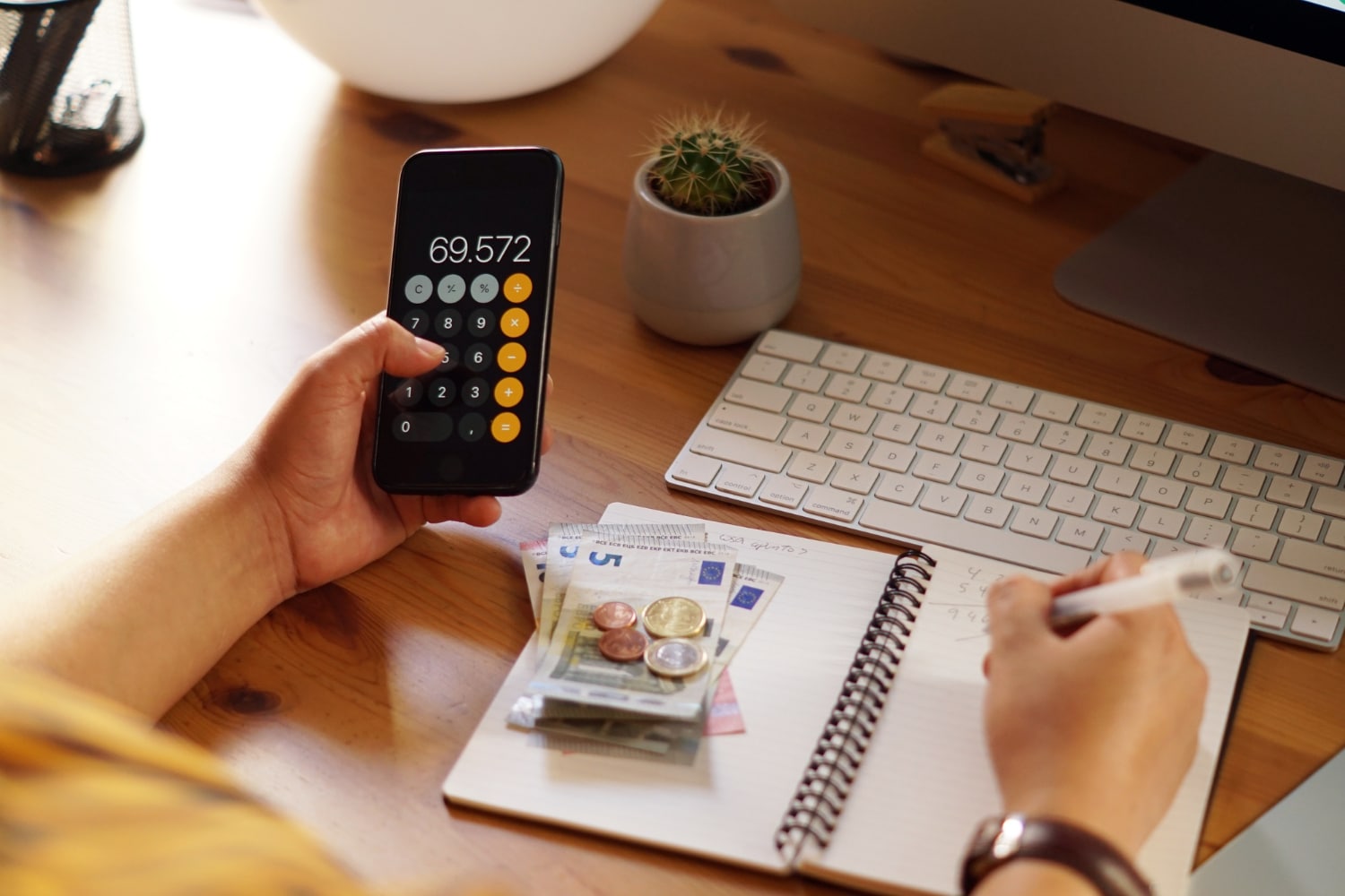pessoa calculando valores com uma calculadora de celular e anotando em um caderno