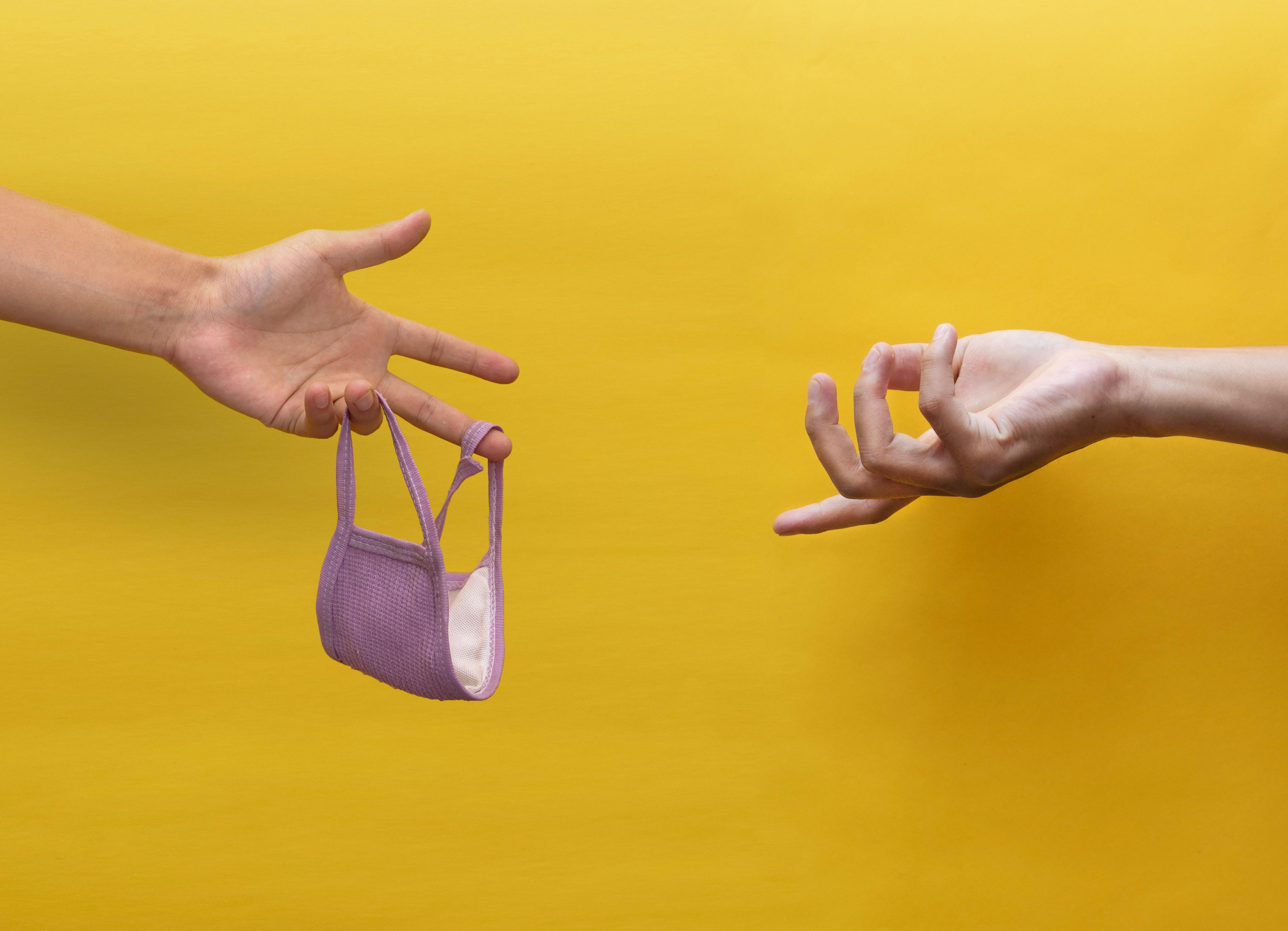 mão estendendo uma máscara à outra em um fundo amarelo