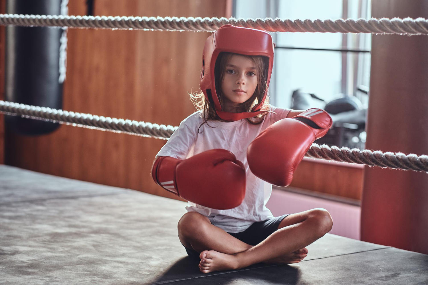 Criança com equipamentos de boxe sentada no ringue de boxe.