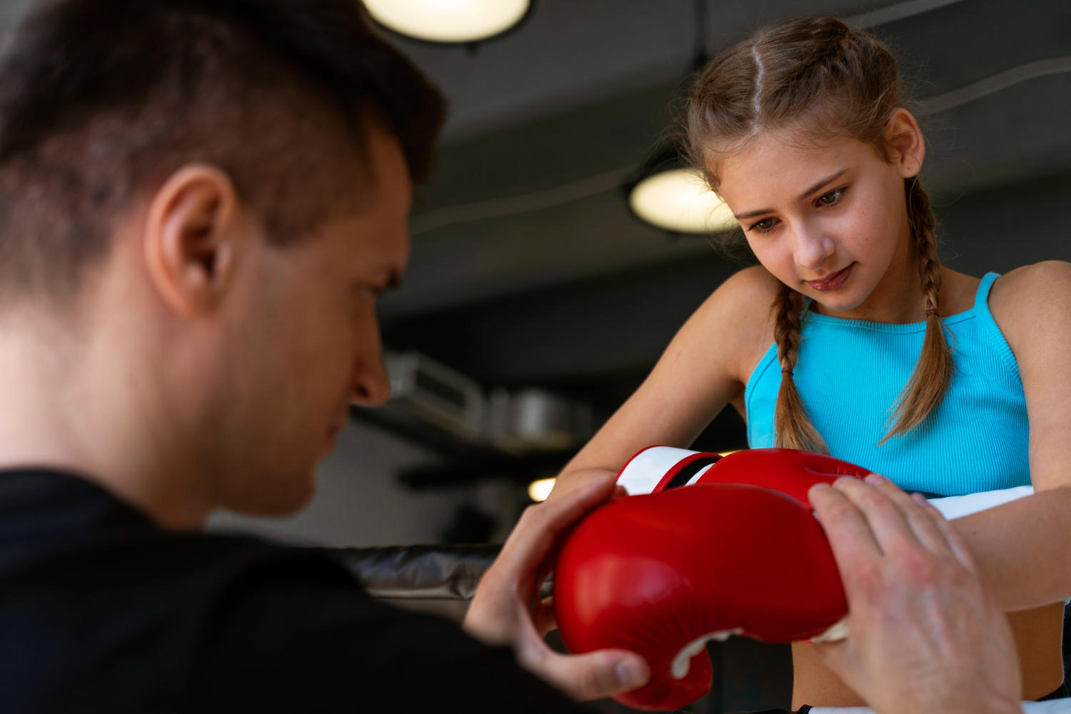Professor ensinando a aluna a colocar as luvas de boxe. 