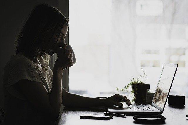 Mulher digita no computador e toma café em preto e branco.