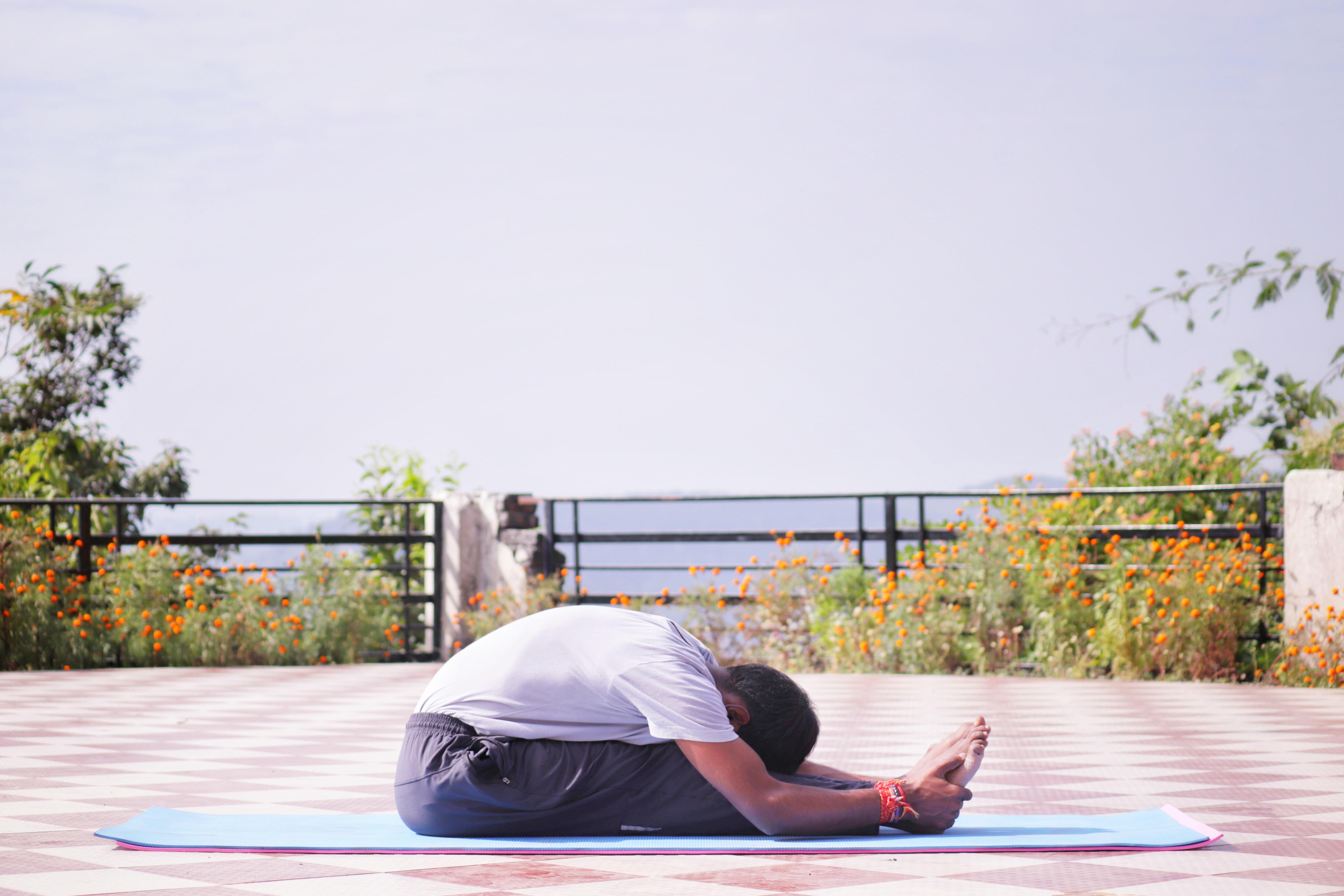 Homem realizando a postura da pinça de yoga ao ar livre.