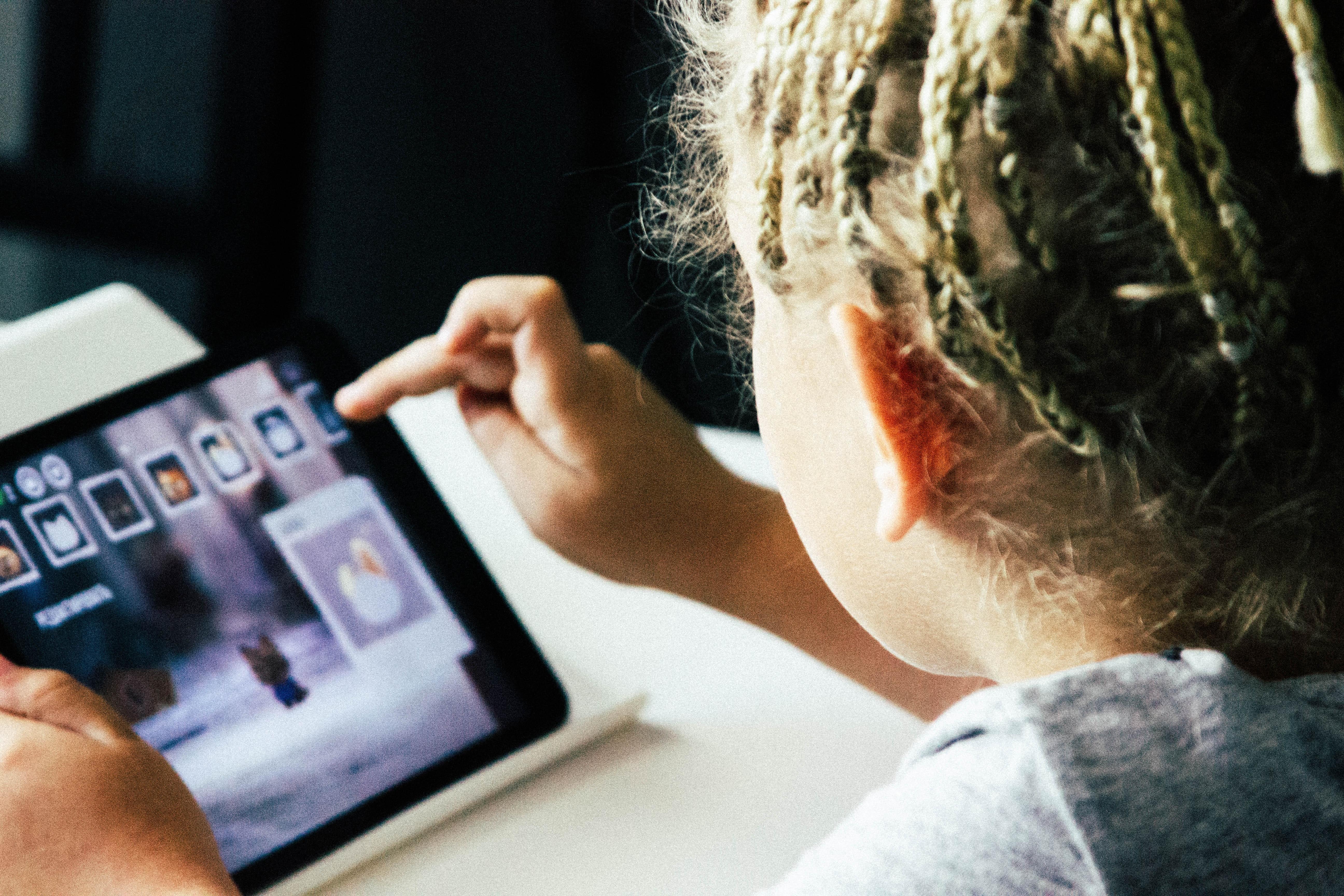 Menina, de costas para a câmera, está a selecionar aplicativos em um tablet.